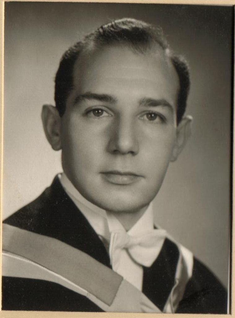 Black and white photo of a young man wearing a white tie and graduating robes. The young man looks slightly right of the camera