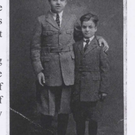 Black and white photo of two small children standing next to eachother. They are wearing suits and the older child has his hand around the younger child's shoulders