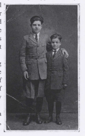 Black and white photo of two small children standing next to eachother. They are wearing suits and the older child has his hand around the younger child's shoulders