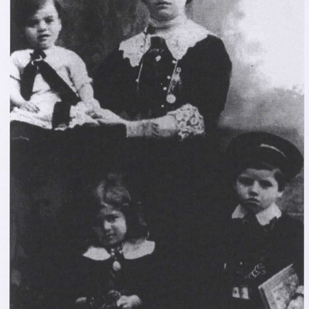 Black and white photo of a mother and three children. They are all dressed up in nice clothes with white collars