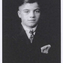 Black and white photo of a young man wearing a suit jacket and tie. He has a pocket square