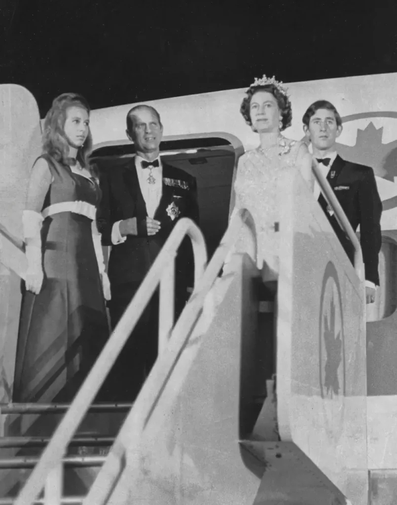 A black and white photo of four people standing at the top of a staircase about to enter an airplane