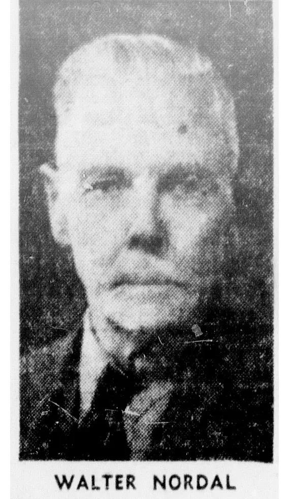Black and white photo of an older man who wears a suit and tie. He looks directly into the camera