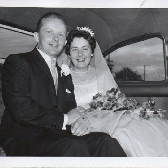 Black and white photo of Jim and Betty Anne Gaynor's wedding. They are seated in the back of a car and are smiling at the camera