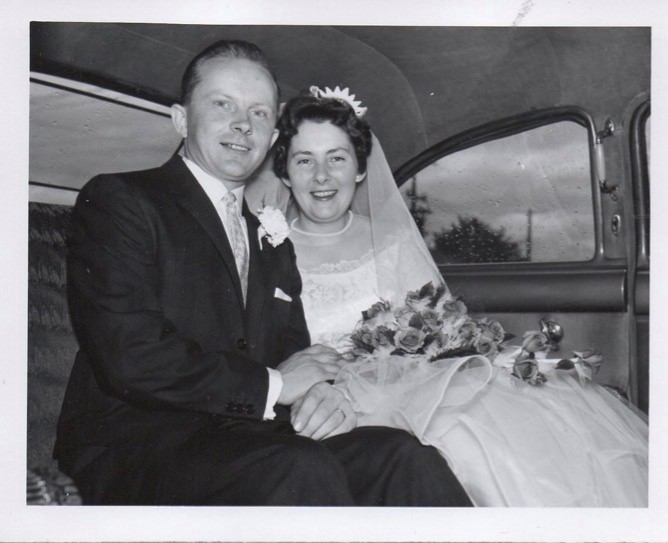 Black and white photo of Jim and Betty Anne Gaynor's wedding. They are seated in the back of a car and are smiling at the camera