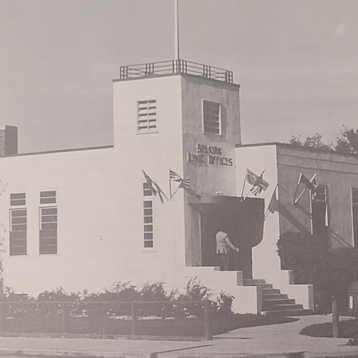 Civic Office, 1957, Selkirk Museum Collection Black and white photo of Civic Office. The building is white and has a flag pole on the top. There are smaller flags on the wall around the entrance to the building