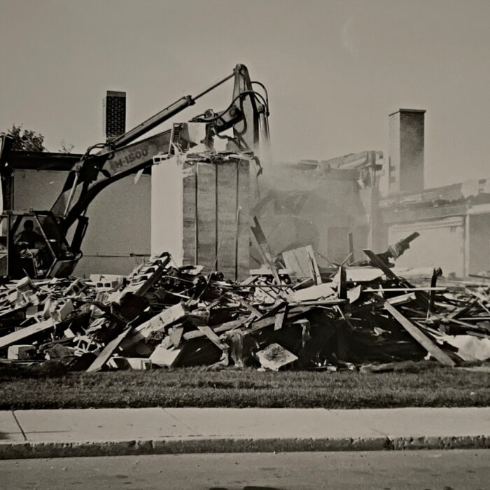 Demolition of the Selkirk Civic Office East Wing, 1983, Selkirk Enterprise Black and white photo of the demolition of the old Civic Office. There is an excavator on the left side of the photo and lots of rubble and dust at the center of the frame.