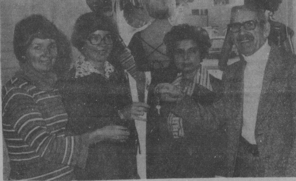 Black and white photo of a group of people standing together. They are dressed up and ceremoniously hand over the keys to a building symbolizing an ownership change