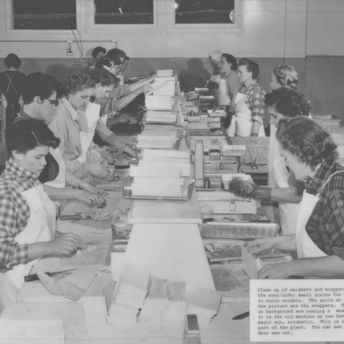 Close-up of Weighers and Wrappers at Booth Fisheries, 1934-1935, Booth Fisheries Black and white photo of a group of people along a table weighing and wrapping fish