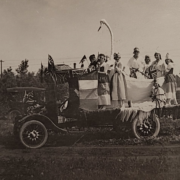 Float with Women Dressed as other Countries Flags, 1919, Selkirk Museum Collection Black and which photo of a parade float with a group of women standing on the back of the truck