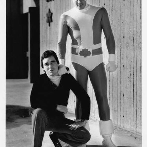 Black and white photo of Richard Comely crouching next to a man dressed as Captain Canuck