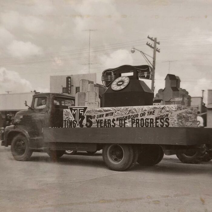 Selkirks 75th Parade MTS, 1957, Selkirk Museum Collection Black and white photo of the MTS parade float. There is a large rotary style phone on the back of a flat deck truck