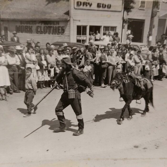 Selkirks 75th Parade Man and Horse, 1957, Selkirk Museum Collection Black and white photo of a group of people standing watching a parade. There is a man leading a pony down the road