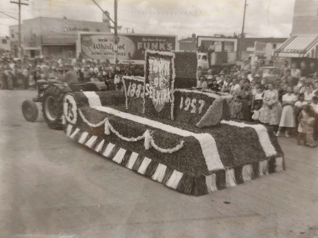 Black and white photo of the Town of Selkirk's parade float. The floar is decorated with flowers and a long banner which runs the length of the flat deck trailer