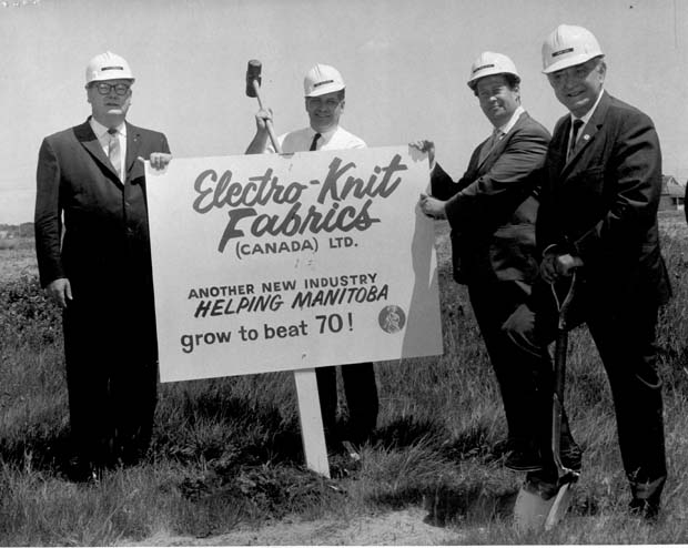 Black and white photo of a group of men in hard hats holding up a sign that reads Electro-Knit Fabrics